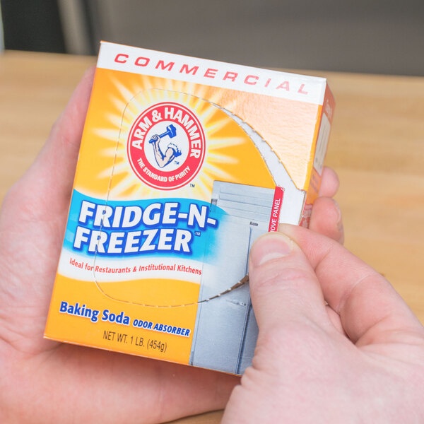 A person holding a box of Arm & Hammer Fridge-N-Freezer Baking Soda on a counter.