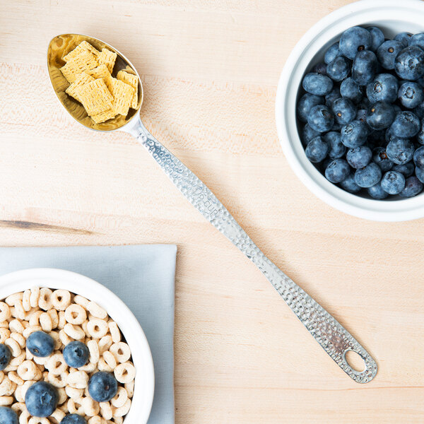 A spoon in a bowl of cereal and blueberries with the American Metalcraft Hammered Stainless Steel Portioned Server.