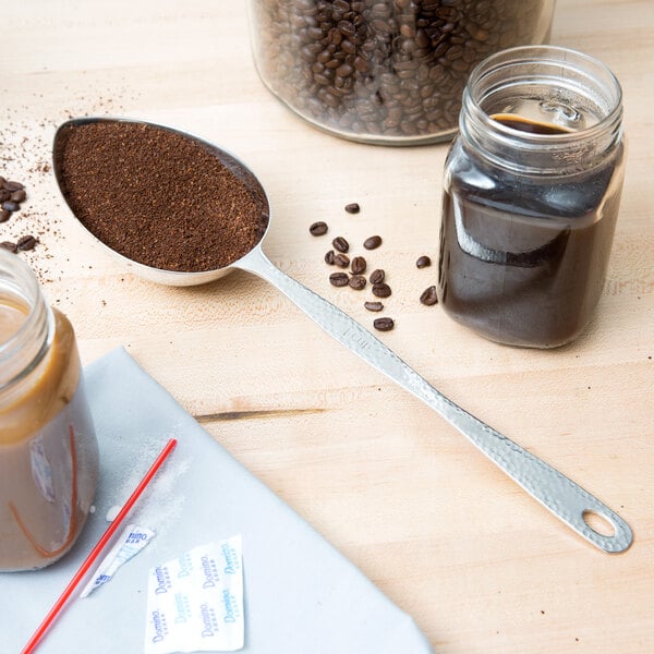 A spoon with ground coffee and a jar of coffee beans on a table.
