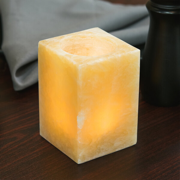 A Sterno alabaster square liquid candle holder with a candle inside on a table.