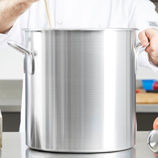 A chef stirring a large Vollrath Wear-Ever aluminum stock pot.