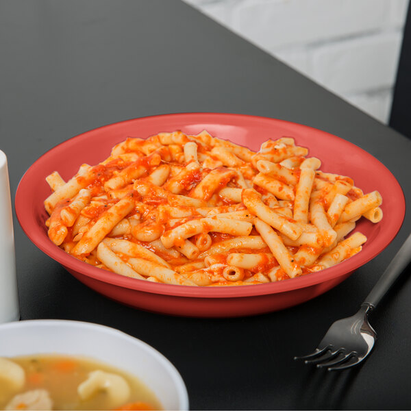 A Rio orange melamine bowl filled with pasta and sauce with a fork on the side.