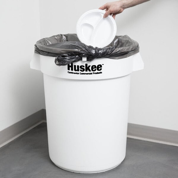 A person holding a white Continental Huskee round trash can.