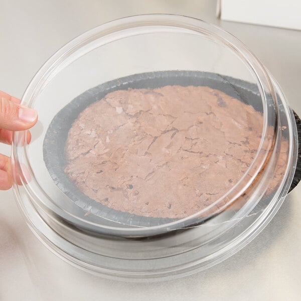 A hand holding a clear plastic container with a brown cake inside.