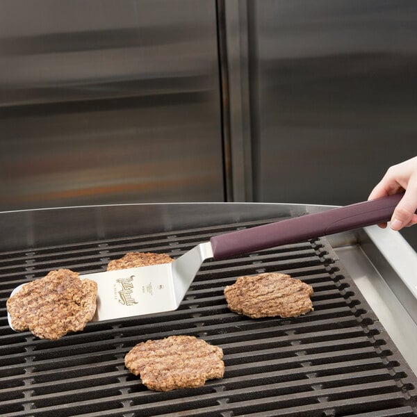A person using a Mercer Culinary Hell's Handle spatula to cook hamburgers on a grill.