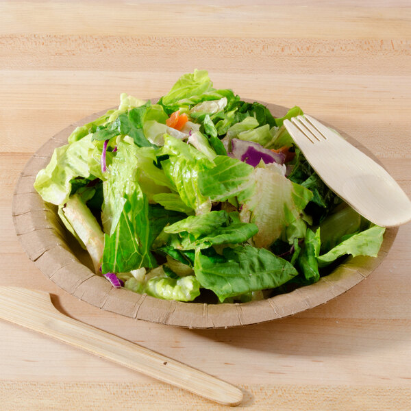 A bowl of salad with a wooden fork on a table with a Solut Coated Kraft Paper Plate.