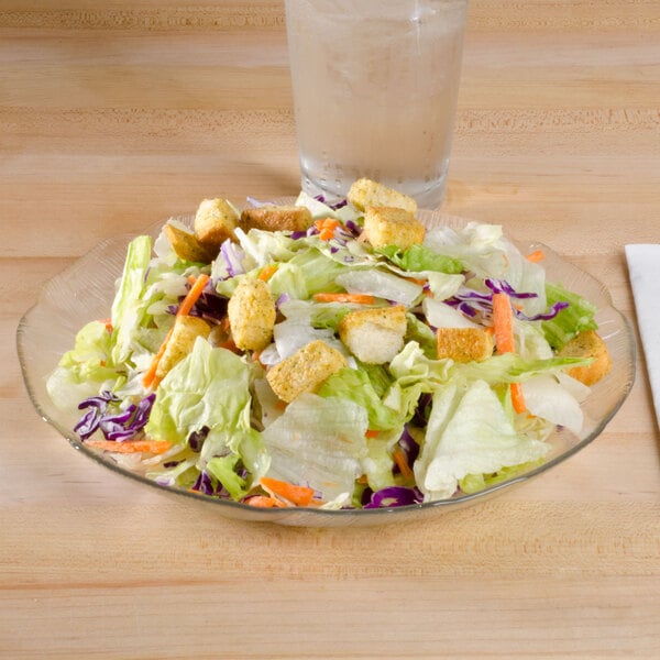 A salad on an Arcoroc Fleur glass plate next to a glass of water.