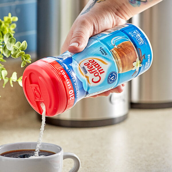 A hand pouring Nestle Coffee-Mate French Vanilla powder into a cup of coffee.