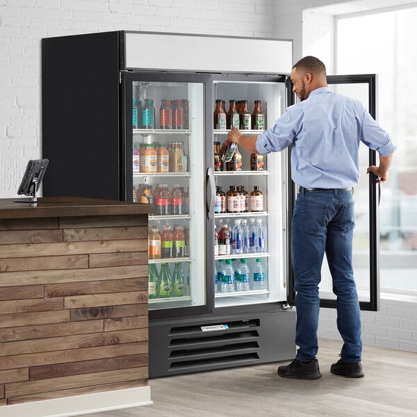 A man standing next to a Beverage-Air refrigerated glass door merchandiser with drinks inside.