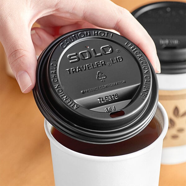 A hand placing a black Solo Traveler plastic lid on a cup of coffee.