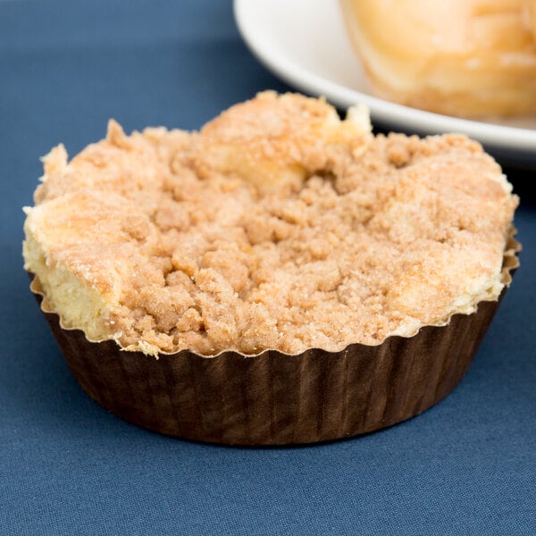 A Solut paper baking cup filled with a small muffin with a crumb topping on a blue plate.