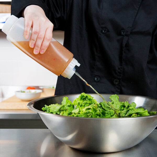 A hand using a FIFO Innovations squeeze bottle to pour sauce onto a bowl of lettuce on a counter.