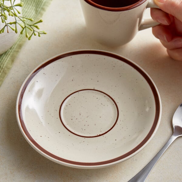 A person holding an Acopa brown speckle narrow rim saucer with a cup.