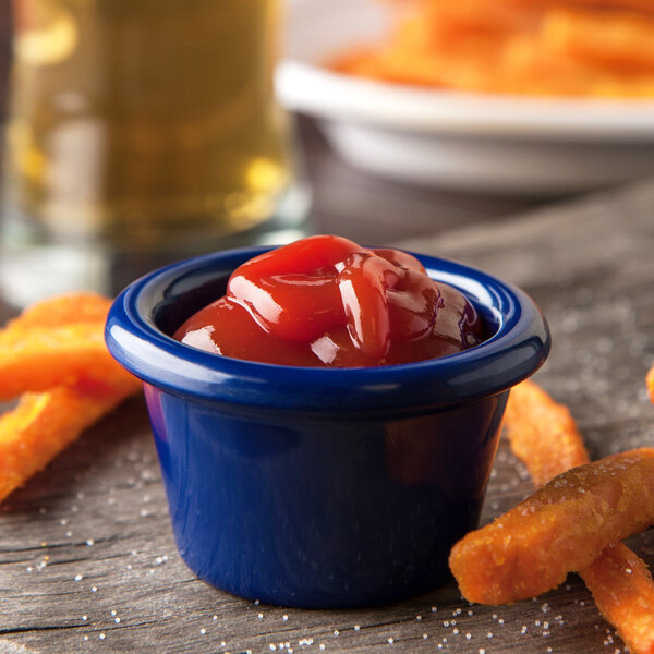A bowl of ketchup and French fries served in a Carlisle cobalt blue melamine ramekin.