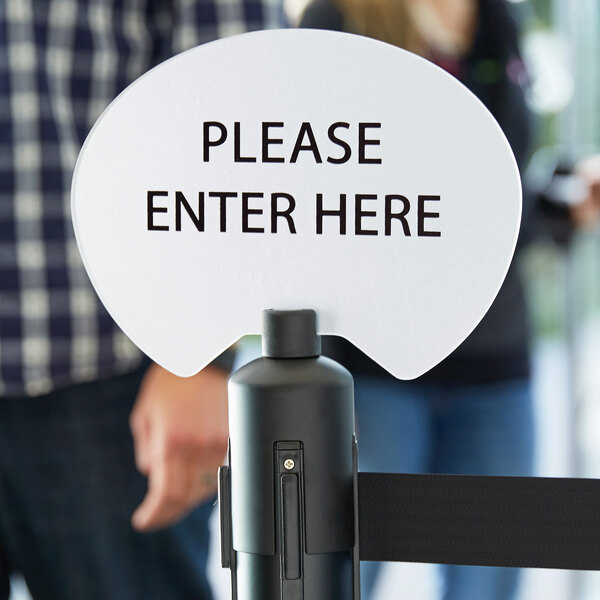 A white oval sign with black text that says "Please Enter Here" on a black cylinder.