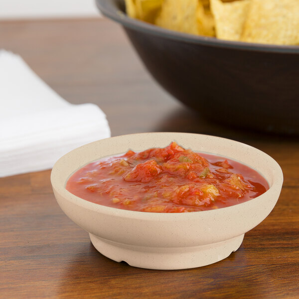 A sandstone bowl of salsa and chips on a table.