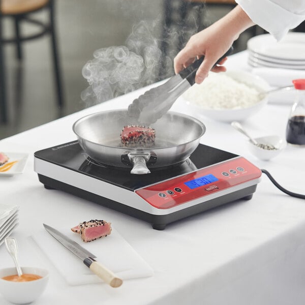 A person cooking food in a pan on an Avantco countertop induction range.