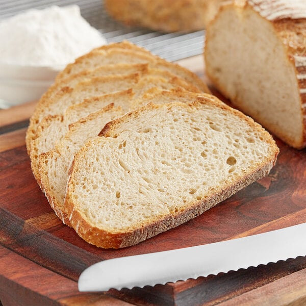 A slice of bread with a white strip on a cutting board next to a loaf of bread and a pile of ADM High Gluten Flour.
