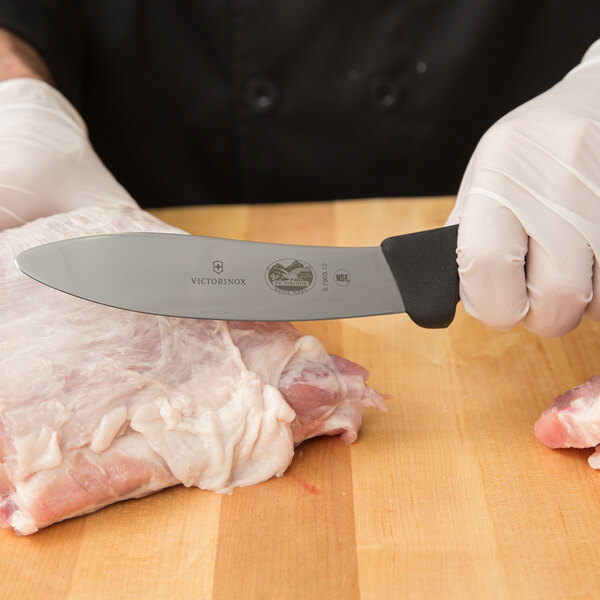 A person in gloves using a Victorinox lamb skinning knife to cut raw meat.