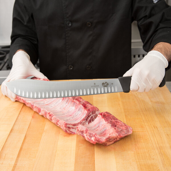 A person using a Victorinox butcher knife to cut a piece of meat.
