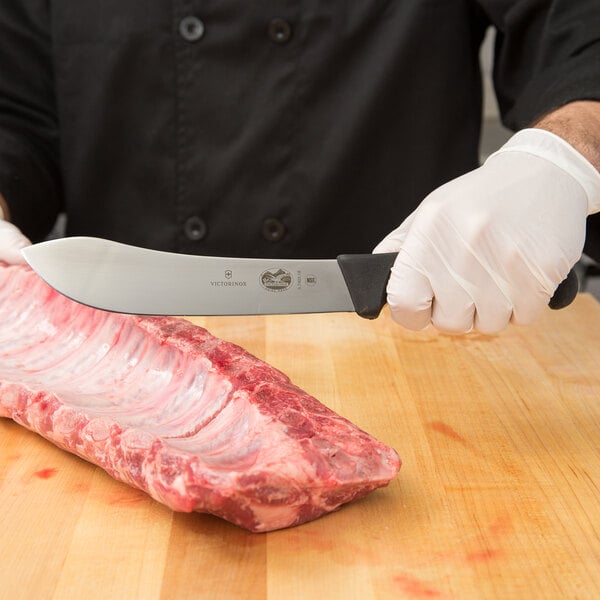 A person in gloves using a Victorinox butcher knife to cut meat.