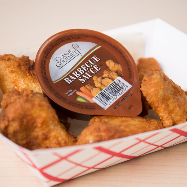 A paper basket of chicken wings with a Classic Gourmet BBQ Sauce portion cup.