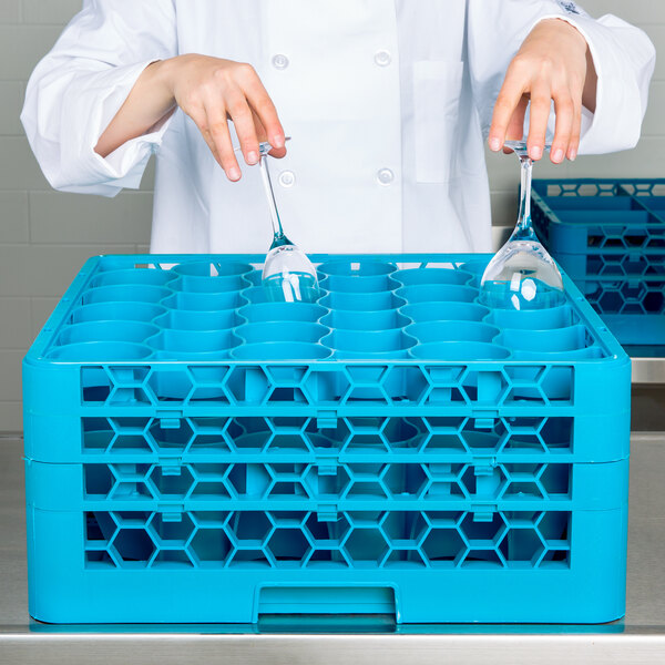 A woman in a white coat using a blue Carlisle glass rack with glasses inside.