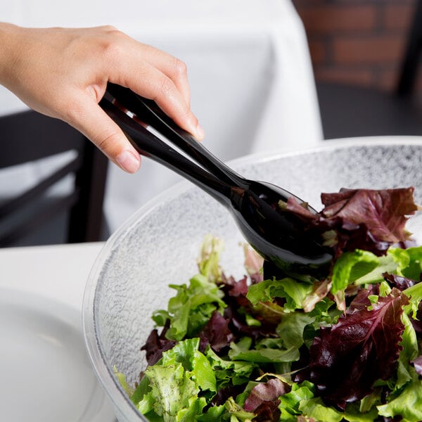A person using Visions black plastic tongs to serve salad