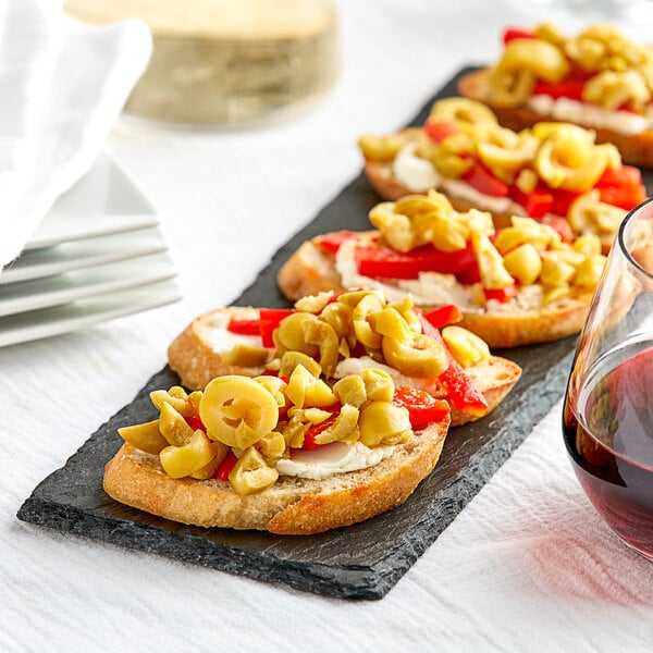 A plate with Manzanilla olives, cheese, and vegetables on toasts next to a glass of wine.