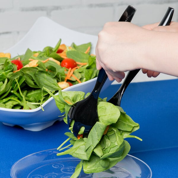 A person using a black Visions disposable plastic serving fork to get salad from a salad bowl.