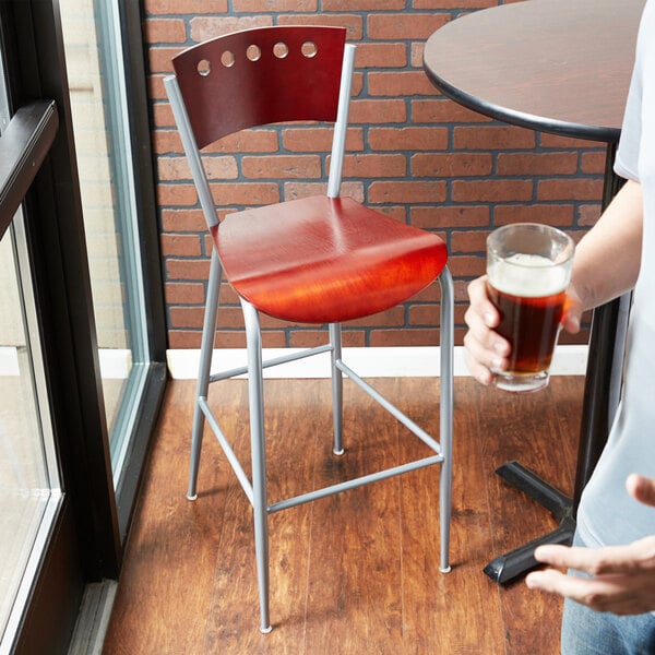A man sitting at a table in a brewery tasting room on a mahogany finish Lancaster Table & Seating cafe bar stool holding a glass of beer.