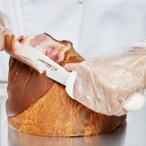 A person in white gloves using a Dexter-Russell lamb skinning knife to cut meat.