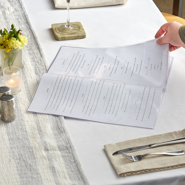 A hand holding a H. Risch, Inc. clear menu cover on a table.