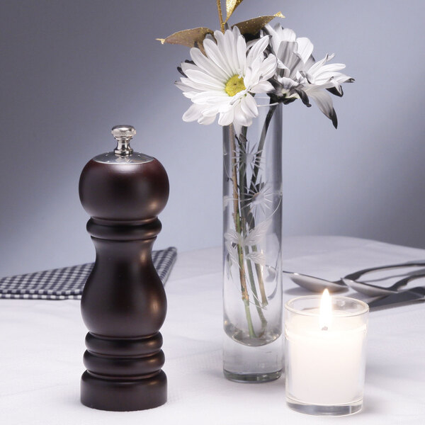 A Chef Specialties black pepper mill and salt shaker combo on a table with a candle and a vase of flowers.