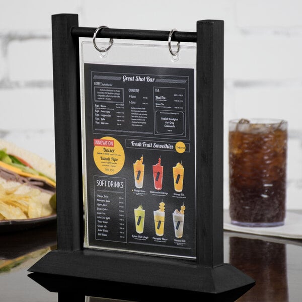 A black Menu Solutions wood table tent holding a white menu on a table with a drink.