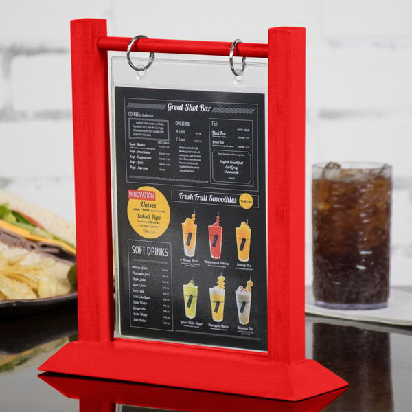 A Menu Solutions wood table tent with a plastic sheet and rings holding a menu on a table with a sandwich and a glass of soda.