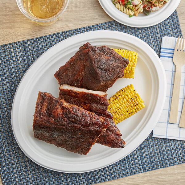 An EcoChoice Bagasse oval platter with ribs and corn on a white table.