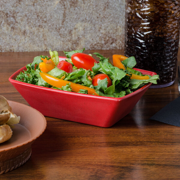 A GET matte red boat bowl filled with salad on a table.