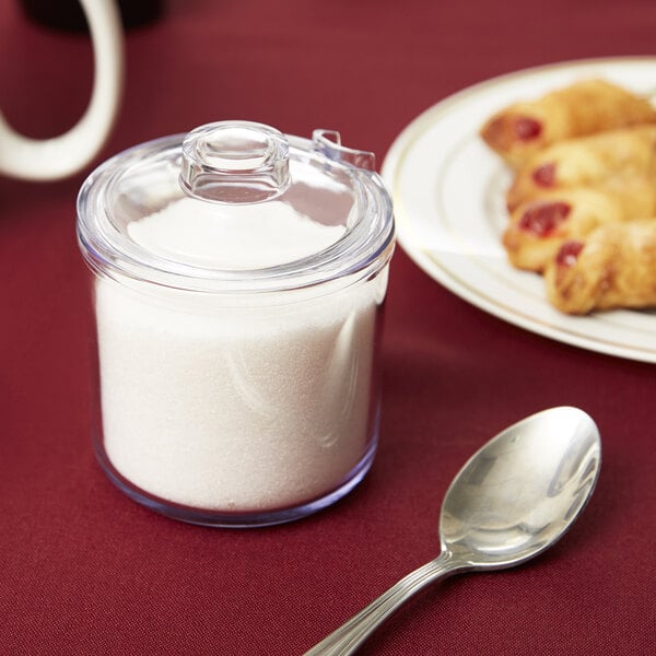 A clear glass jar with a lid filled with sugar next to a plate of pastries.