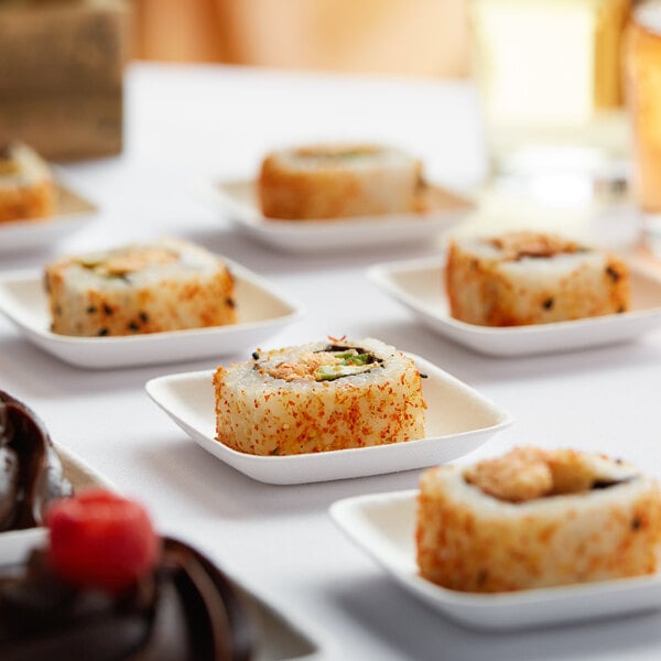 A table with a variety of food items including sushi rolls served on EcoChoice Compostable Sugarcane appetizer plates.