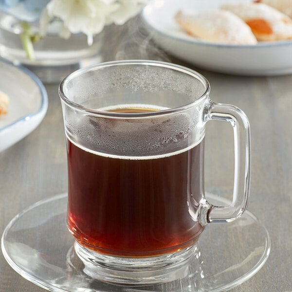 A glass mug of Caffe de Aroma decaf hazelnut coffee on a saucer.