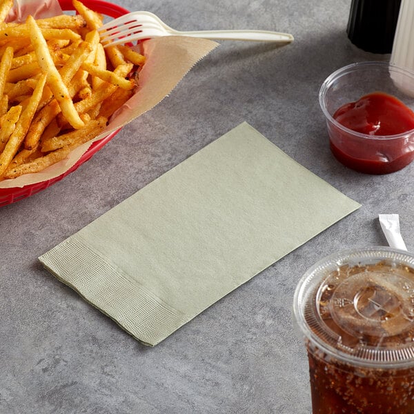 A basket of french fries on a table next to a container of ketchup and a Sage paper dinner napkin.