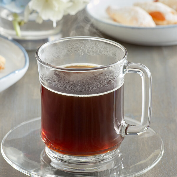A glass mug of Caffe de Aroma Decaf Caramel Cream coffee on a saucer.