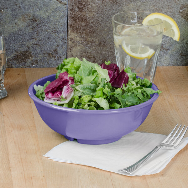 A purple melamine salad bowl with salad and a glass of water on a table.
