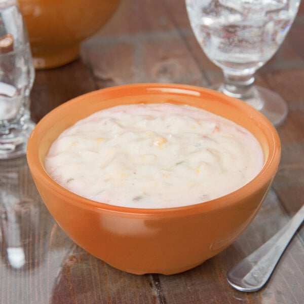 A pumpkin melamine bowl filled with soup on a table with a spoon.