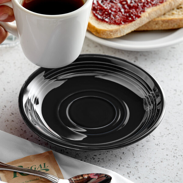 A hand holding a white cup of coffee over a black saucer with jam