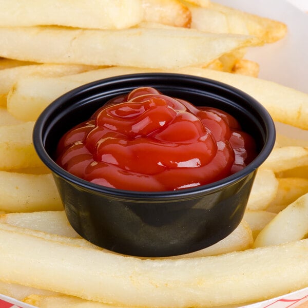 A Solo black polystyrene portion cup filled with ketchup on french fries.