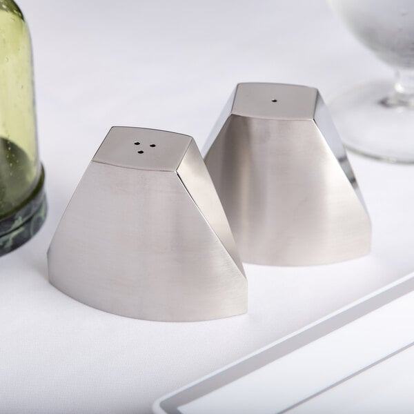 An American Metalcraft stainless steel wedge salt and pepper shaker set on a table next to a glass.