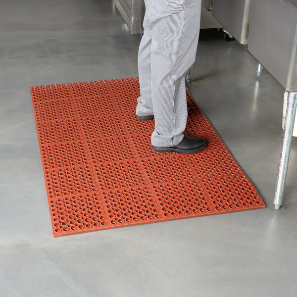 A person standing on a red Cactus Mat anti-fatigue floor mat.