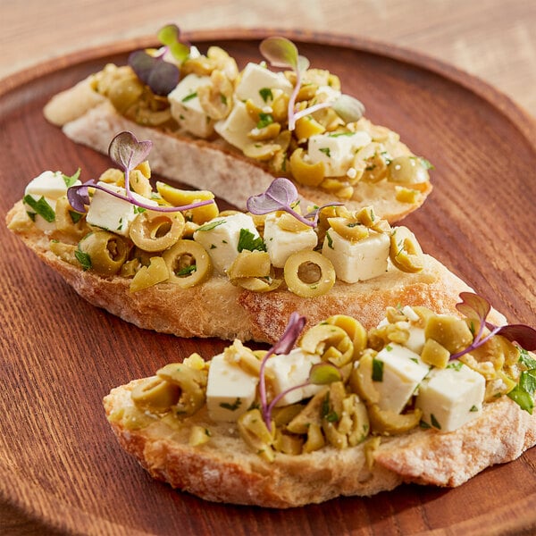 Two slices of bread with Pitted Manzanilla Cocktail Olives and feta cheese on a plate on a wooden surface.